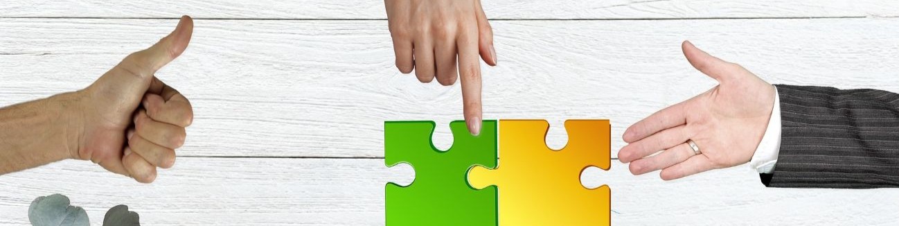 Drei Hände weisen auf zwei verbundene Puzzleteile vor einem Hintergrund aus weißen Holzleisten.